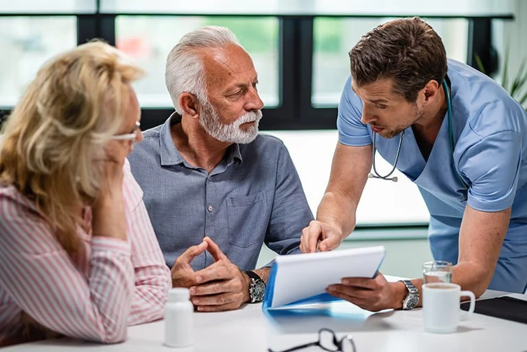 Doctor in blue scrubs discussing sinuplasty options with an older male patient and female companion at a consultation table